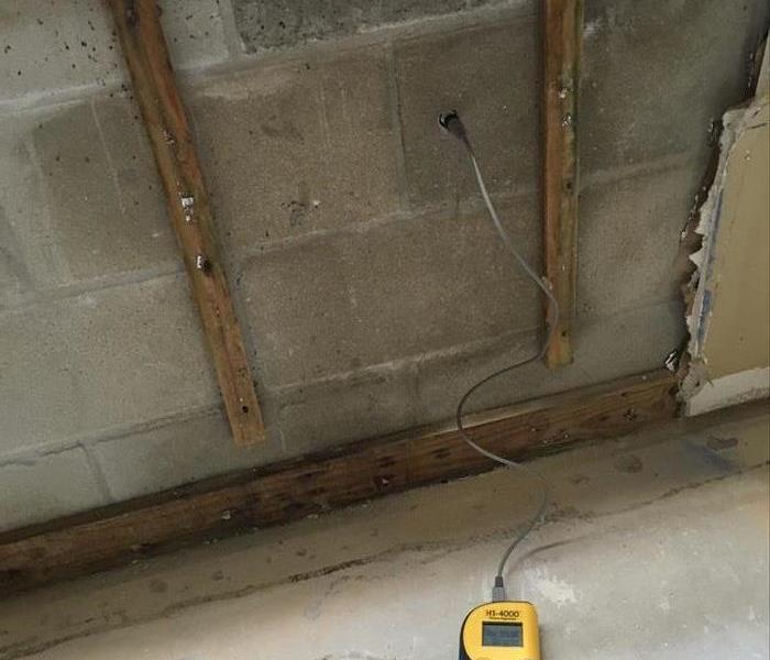 device inspecting the cinder block wall for moisture, fir stripping’s attached, concrete pad