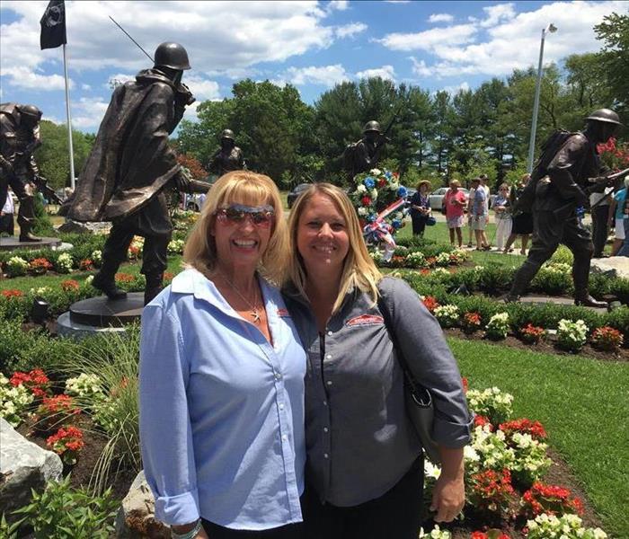 2 women standing in a garden with statues