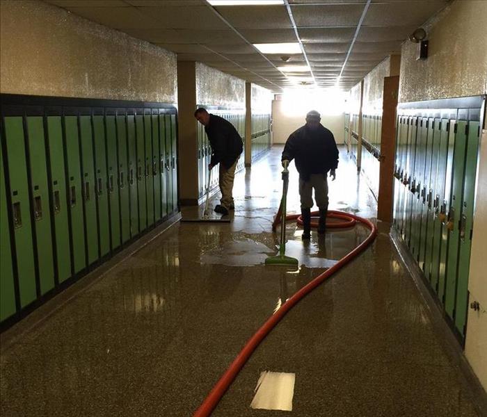 hallway with green lockers and 2 employees working