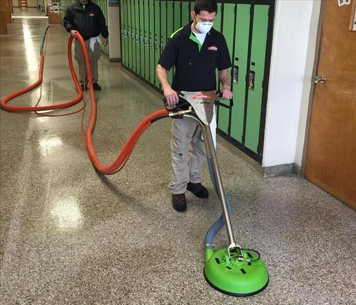 male employee operating a floor scrubber in a school hallway