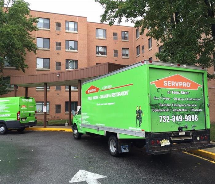 Green SERVPRO trucks in front of a large tan brick building